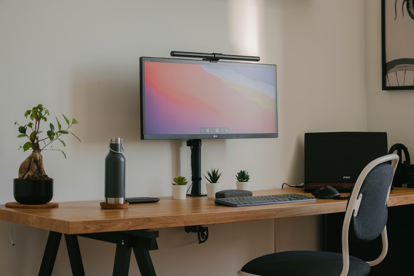 Organized wooden desk with computer, laptop, and plants.