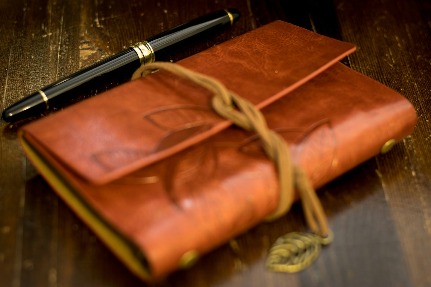 Leather journal with leaf patterns rests on a wooden desk.